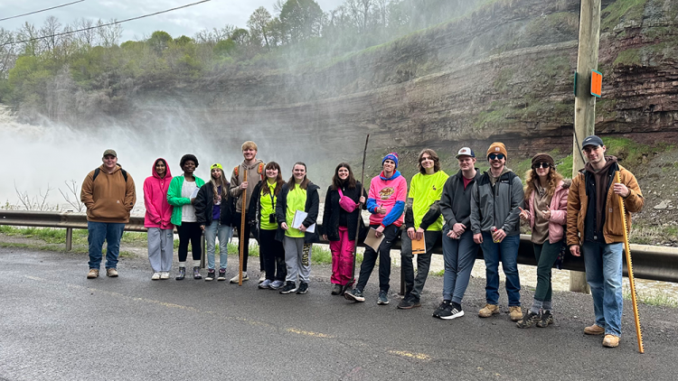 Earth Science Students posing off the side of the road next to a stream