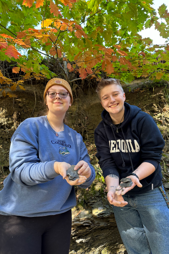 2 Earth Science students smiling and holding up fossilized rocks