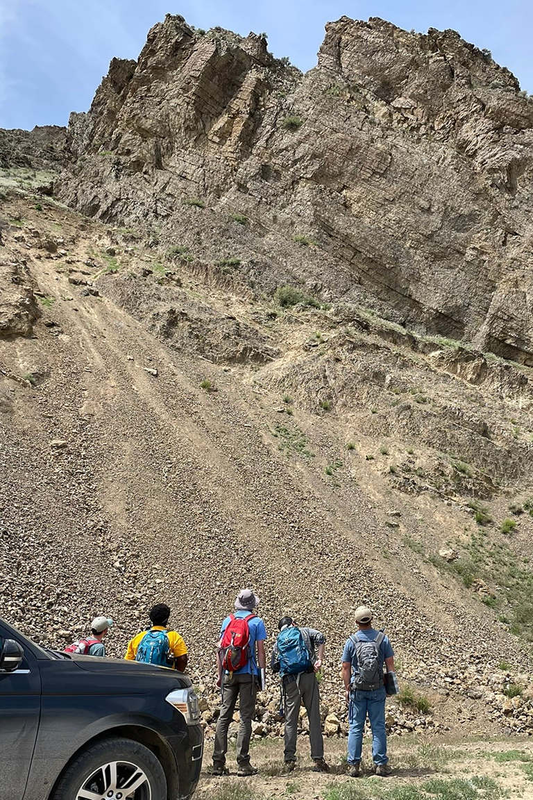 Geology students wearing adventuring gear and facing a large rocky hill
