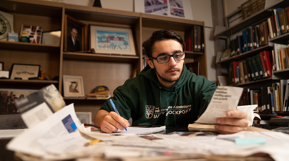 Brockport student reading a news clipping and taking notes in the Rose Archives