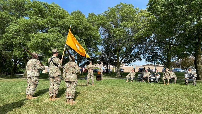 Three Brockport cadets holding a flag while other cadets look on