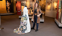 Brockport costume designer and professor stands next to a dress she designed which commemorates famous women in Rochester history