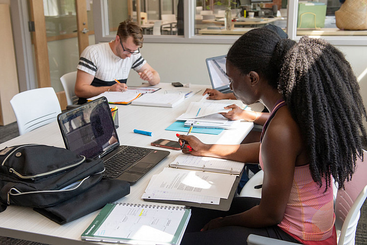 Students studying at a table with notebooks and laptops in the Academic Success Center
