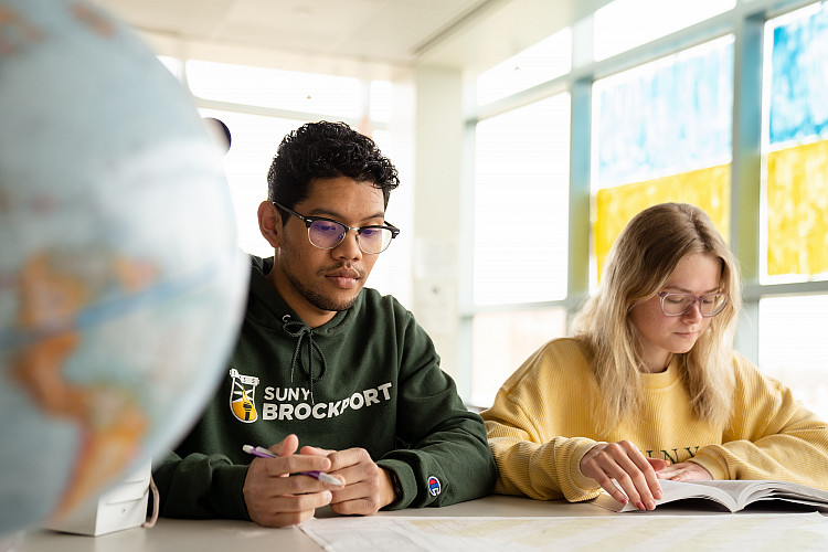 Two students sitting at a desk with a globe next to them