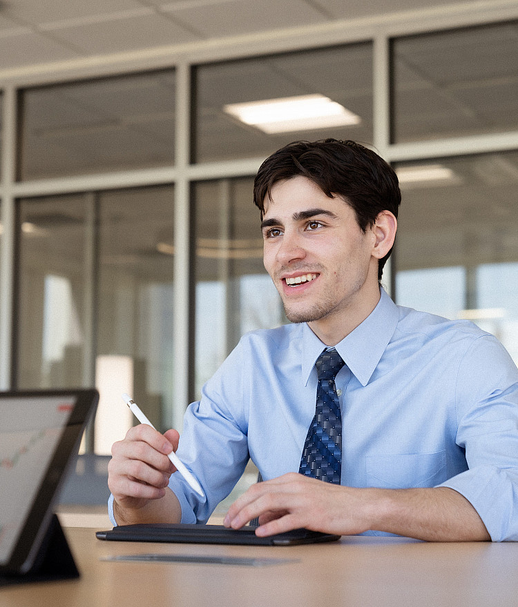 Student dressed in a button down with a tie and talking to someone else at a table
