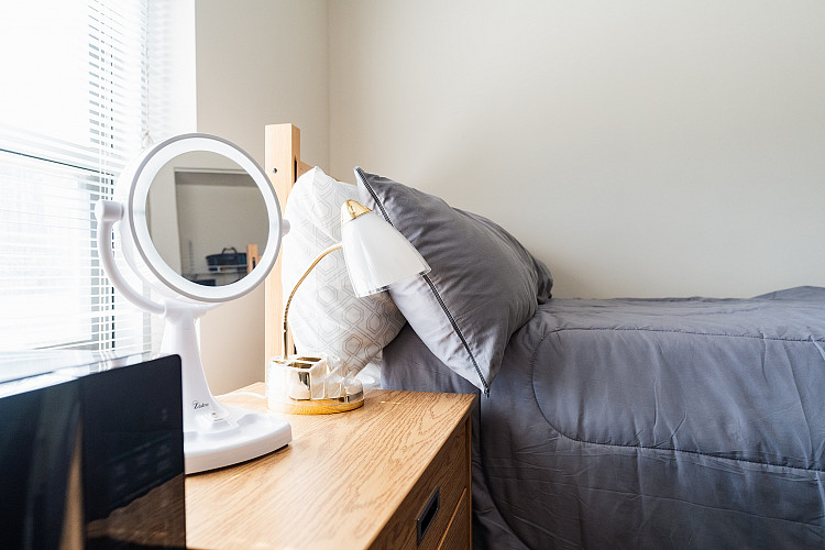 Close up of a dresser and a bed in a corridor style bedroom