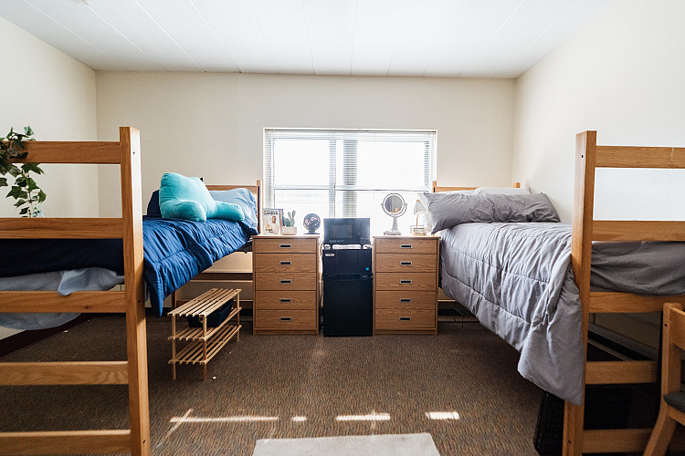 Full view of a corridor style bedroom with 2 beds, 2 dressers, a mini fridge, and a microwave