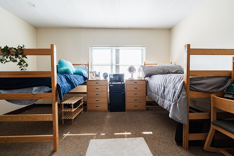 Full view of a corridor style bedroom with 2 beds, 2 dressers, a mini fridge, and a microwave