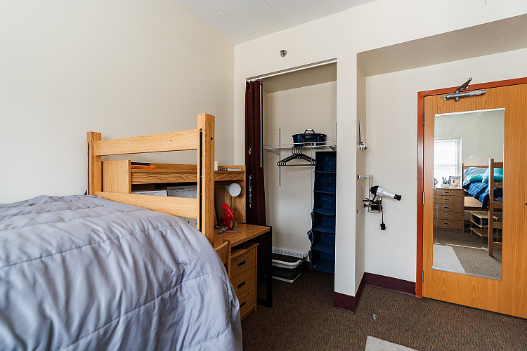 Wide view of a closet space in a corridor style bedroom with a bed and desk to the left
