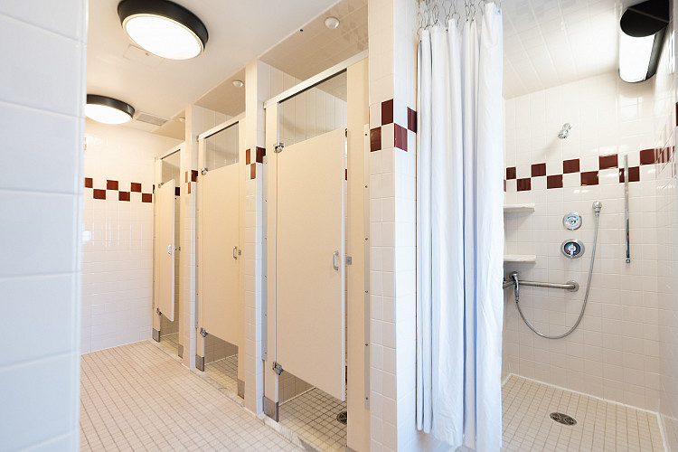 Wide view of corridor style bathroom with 3 bathroom stalls to the left and a shower stall to the right