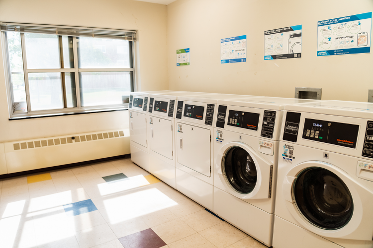 Wide view of corridor style laundry room with 3 dryers and 2 washing machines