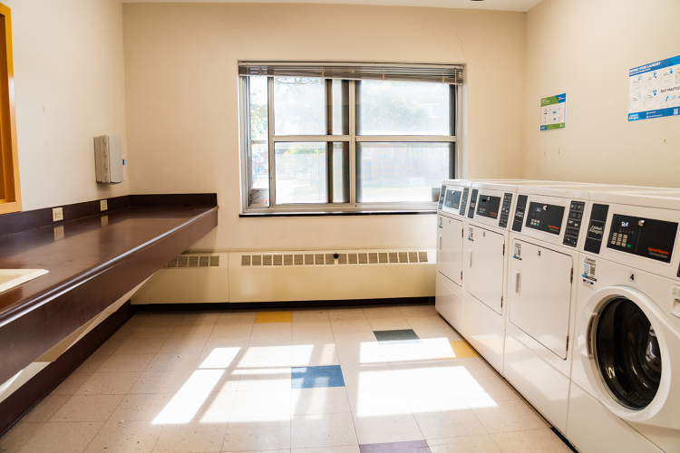 Wide view of corridor style laundry room with a table to the left and drying and washing machines on the right