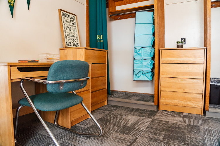 Close up of a desk, chair, dresser, closet space, and another dresser in a corner of a 4 person suite