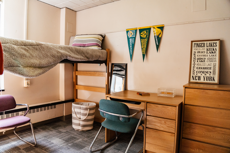 Wide view of lifted bed, desk, chair, and dresser with some decorations in a corner of a 4 person suite