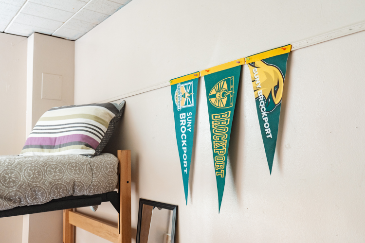 Close up at the head of a lifted bed with SUNY Brockport flags decorated on the wall
