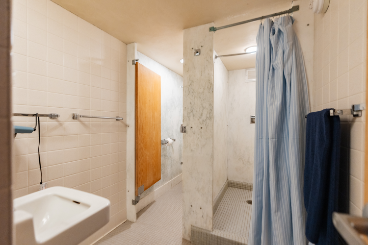 Entrance view of the bathroom of a 4 person suite with a sink to the left, bathroom stall, and shower stall to the right