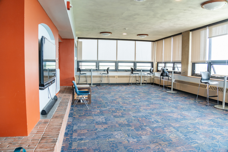 Wide view of a lobby with a wall-mounted TV, tables and high chairs placed throughout