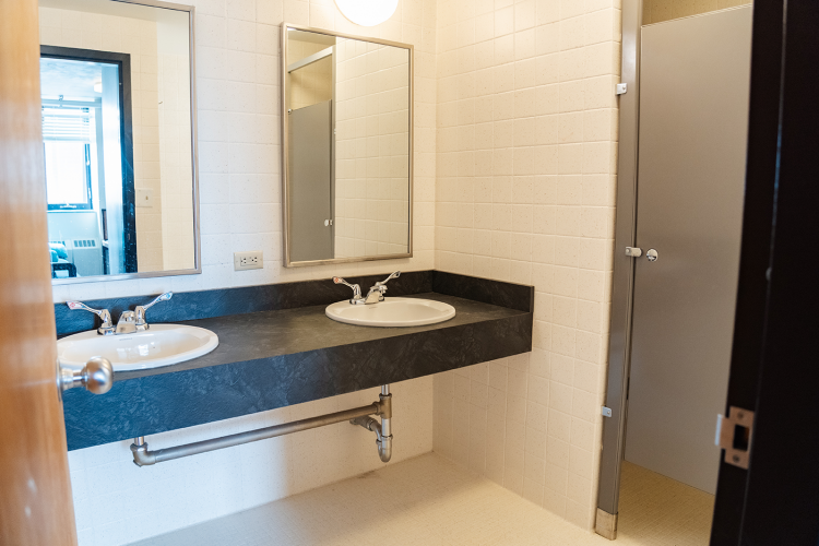 Entrance view of a bathroom with 2 sinks and mirrors and a bathroom stall