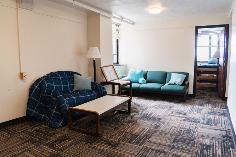 Angled view of a living room with a couch, coffee table, another couch, and an entrance to a bedroom