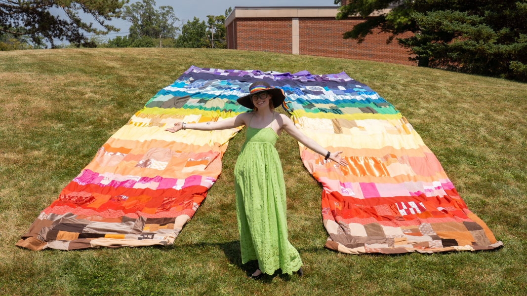 Sophia Berwanger standing in front of a pair of colorful giant pants laying on the grass outside of Lennon Hall.