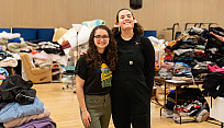 Melissa Syzurgi (left) standing in the Cooper Hall Gym, in front of donations, next to Ashley Cook (right).
