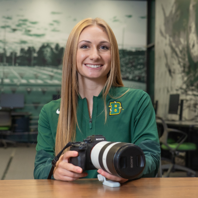 Olivia Metz, a Brockport alum, holding a camera and smiling