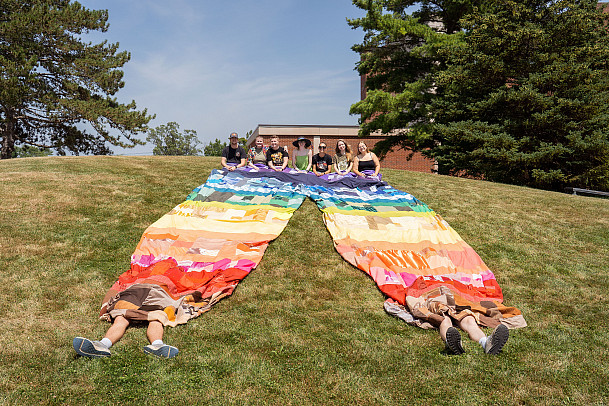 Students seated with Sophia Berwanger, who is showcasing a large pair of pants she crafted from donated textiles.