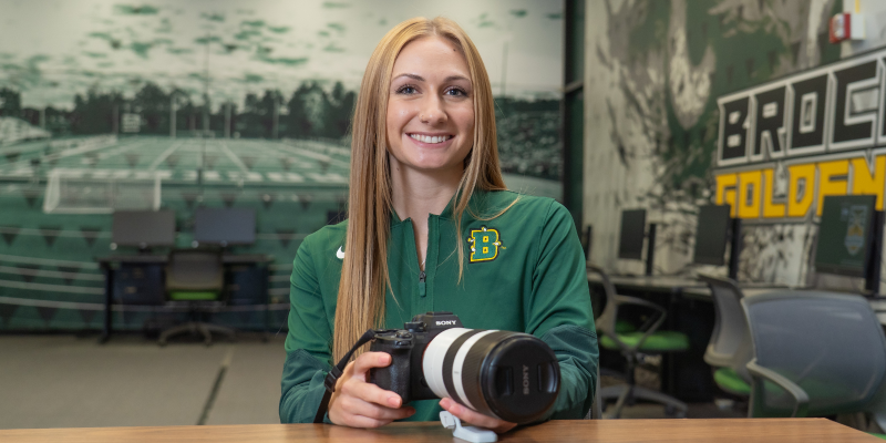 Olivia Metz, a Brockport alum, holding a camera and smiling