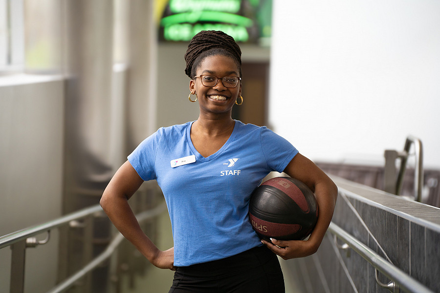 Anaheysha Baptiste-White holding a workout ball and wearing her YMCA uniform.