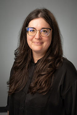 A white woman with glasses and long brown hair wears a black shirt.