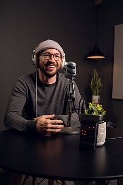 Kyle sits in front of a microphone. *It looks like he is recording a podcast but it is staged for the photo. 